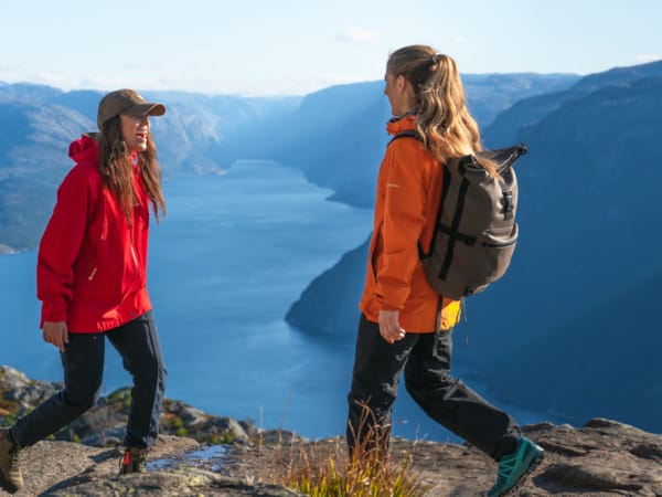 To kvinner i røde jakker og ryggsekker står på et fjell.