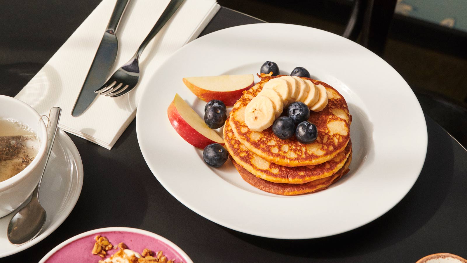Nydelig frokosttallerken med luftige pannekaker dekket med banan og blåbær