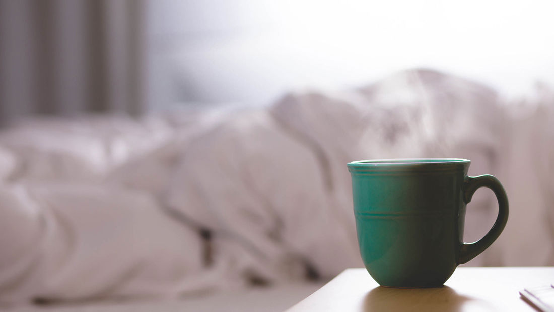 Generisk bilde av hotellerom med uoppredd seng og kaffekopp det ryker fra stående på nattbordet.