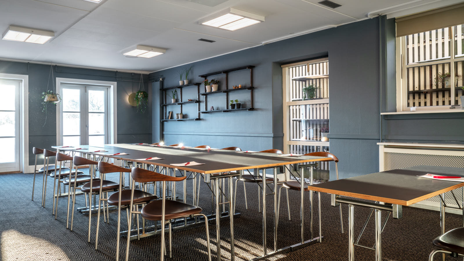 Nærbilde av bord og stoler i klasseromsoppsett. På bordene ligger penn og papir