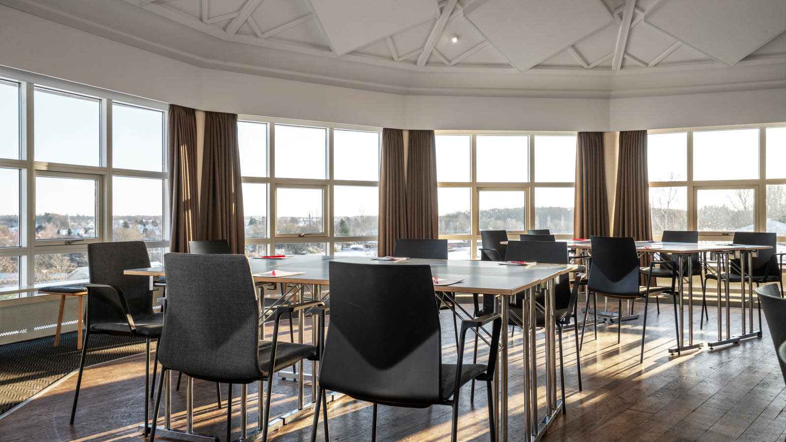 Stort møterom med kuppeltak og store vindusflater. Grupper med bord og stoler.