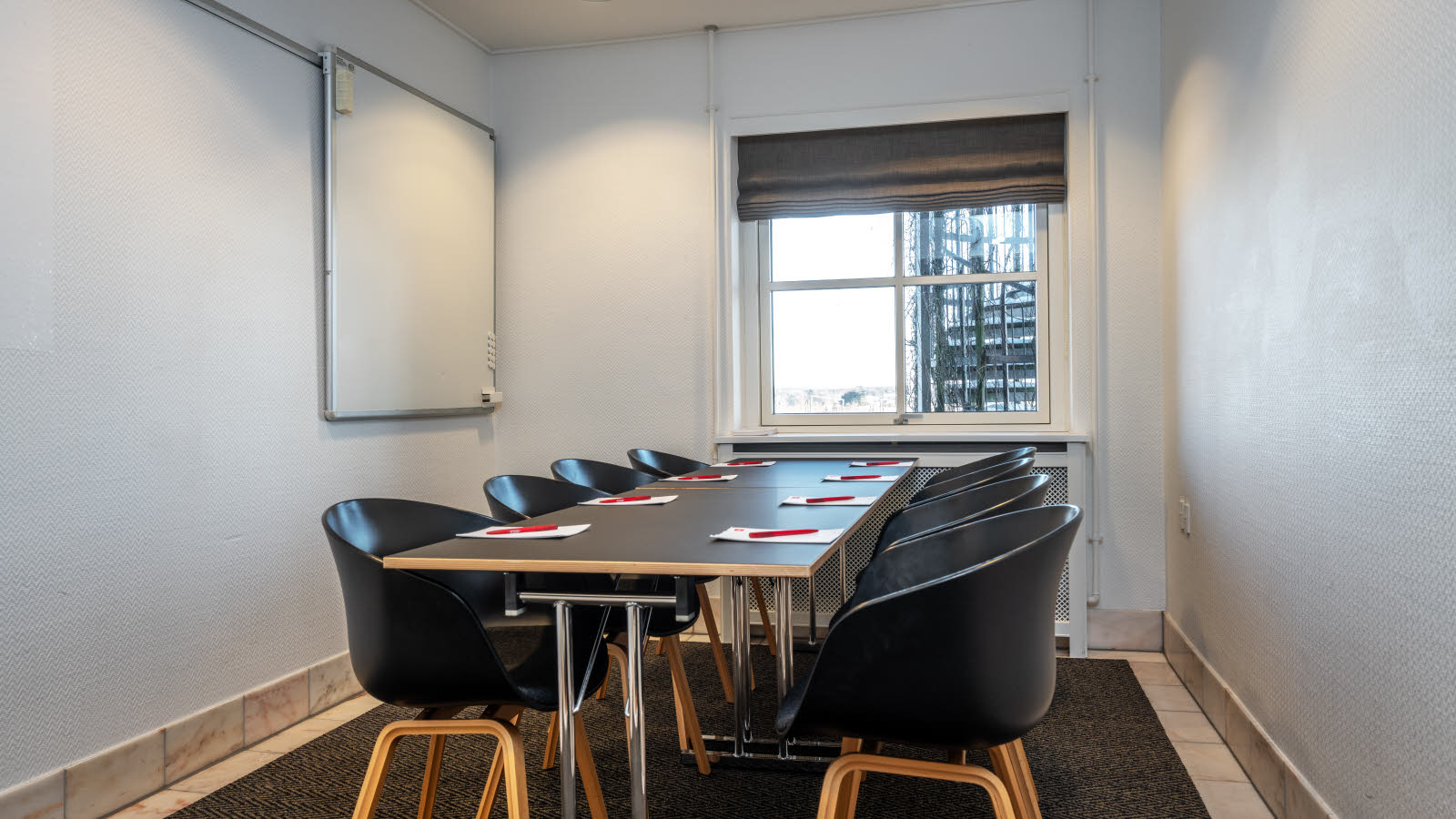 Nærbilde av bord og stoler i klasseromsoppsett. På bordene ligger penn og papir