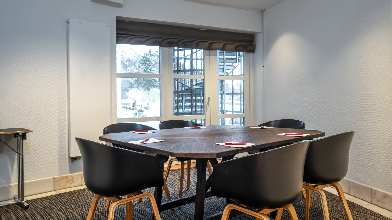 Nærbilde av bord og stoler i klasseromsoppsett. På bordene ligger penn og papir