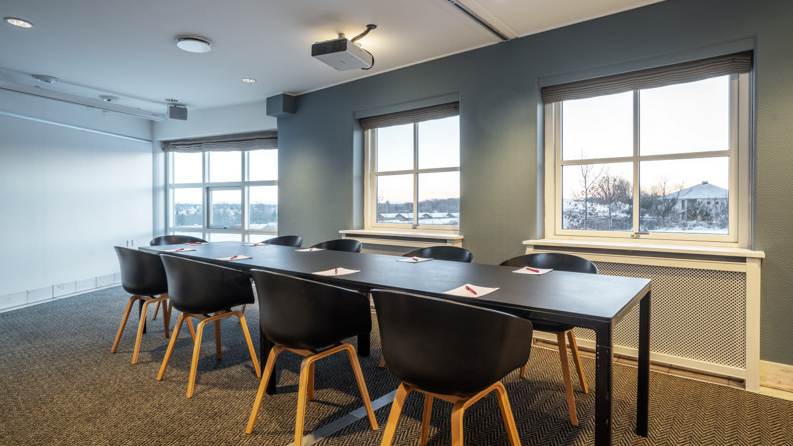 Nærbilde av bord og stoler i klasseromsoppsett. På bordene ligger penn og papir