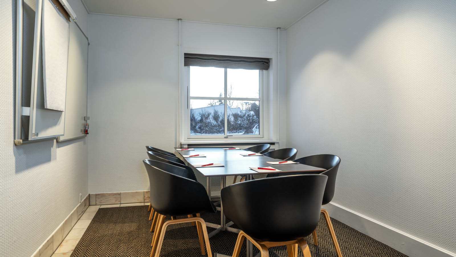 Nærbilde av bord og stoler i klasseromsoppsett. På bordene ligger penn og papir