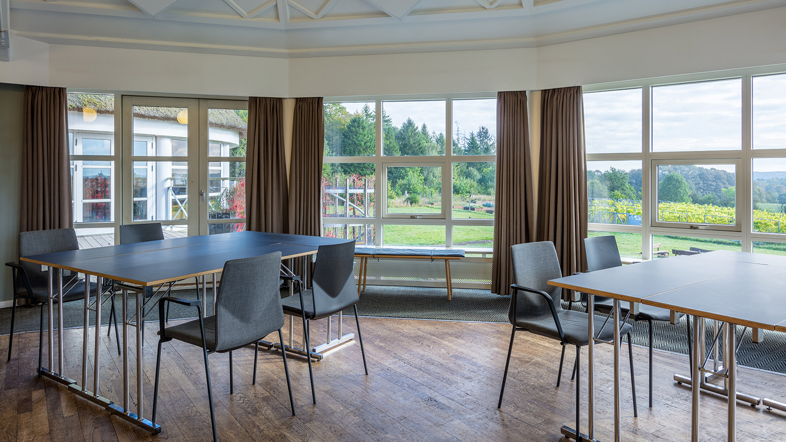 Bord og stoler i grupper i møterom med store vinduer og utsikt mot hage