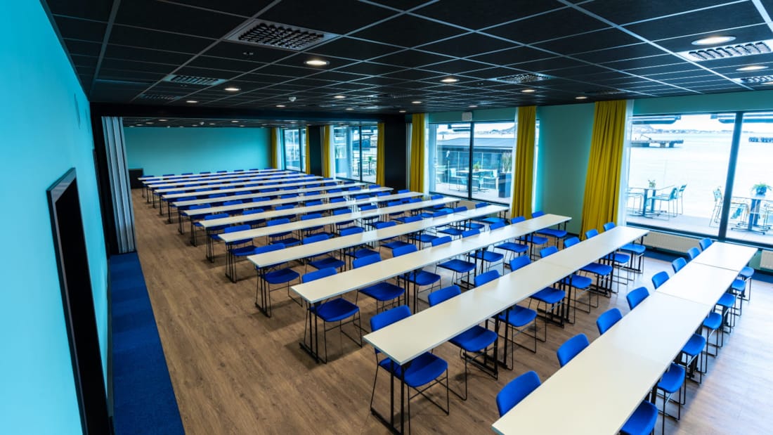 Konferanselokale i klasseromsoppsett med blå stoler og store vinduer