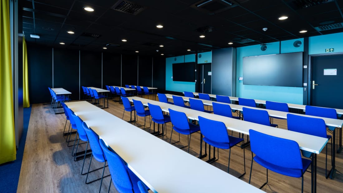 Konferanselokale i klasseromsoppsett med blå stoler og to tv skjermer