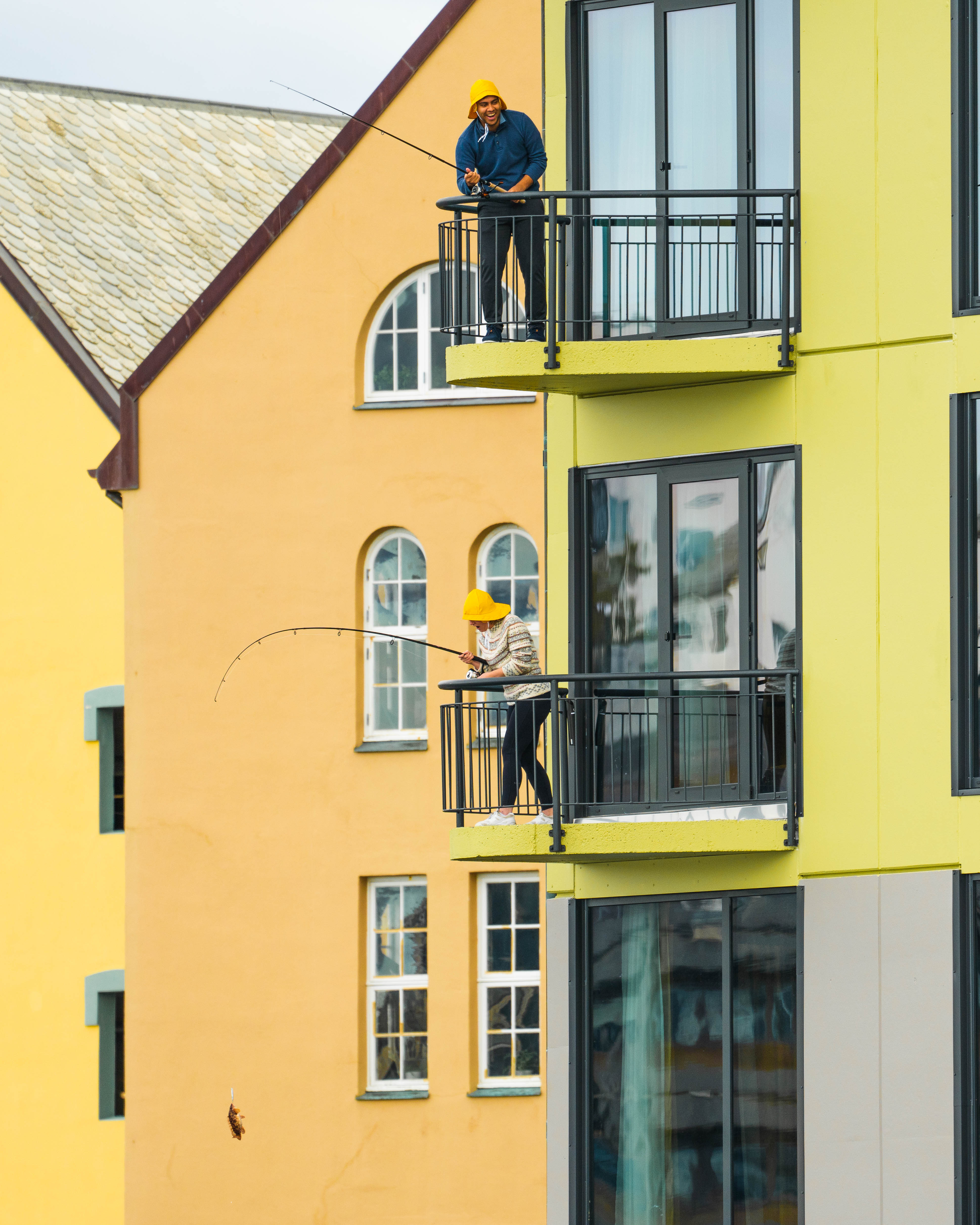 To personer står på hver sin balkong og fisker hos Thon Hotel Ålesund.