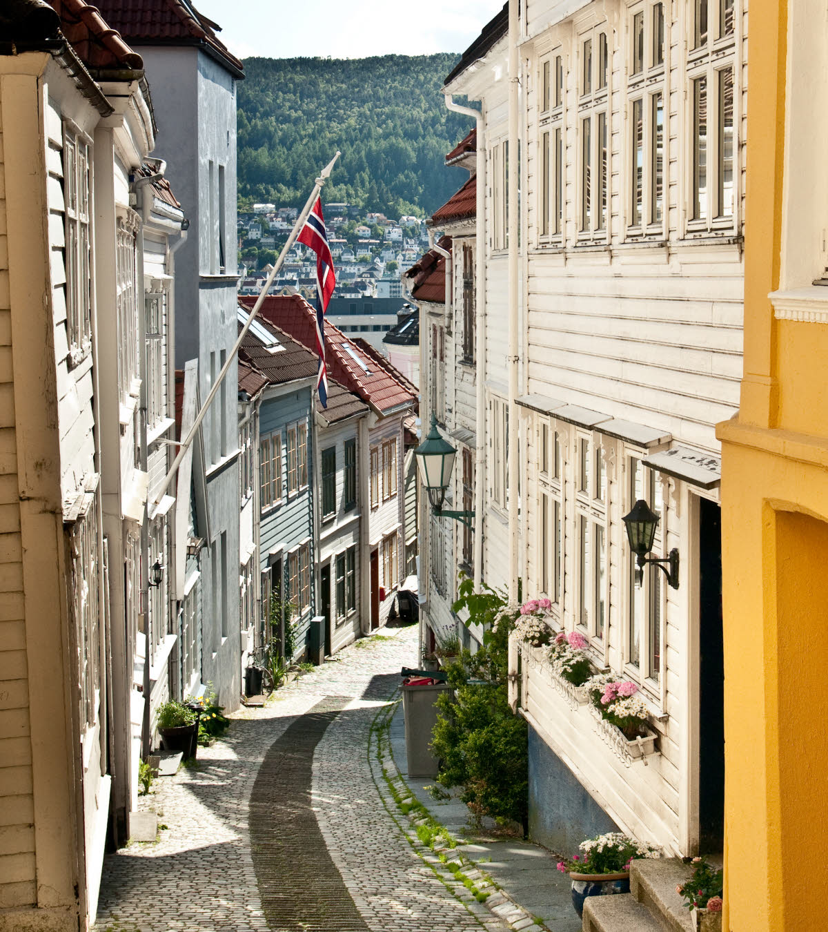 Karakteristisk bratt smug i gamlebyen i Bergen med norsk flagg og skinnende sol.