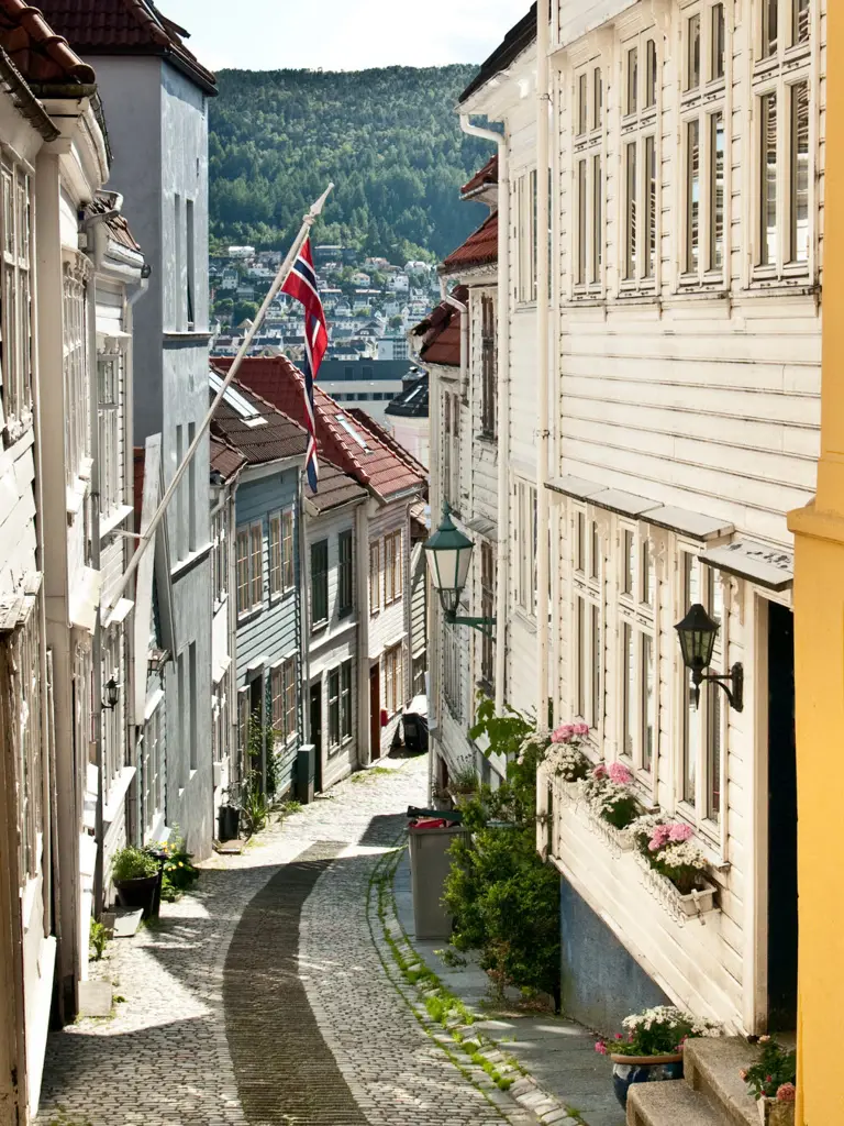 Karakteristisk bratt smug i gamlebyen i Bergen med norsk flagg og skinnende sol.