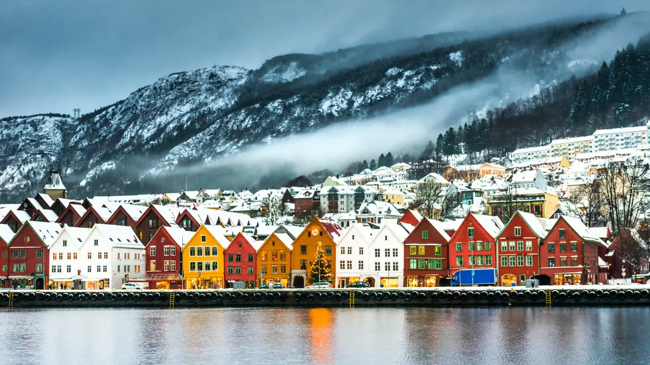 Bryggen i Bergen med snø på takene, og snøflekker i fjellet bak Bryggen.