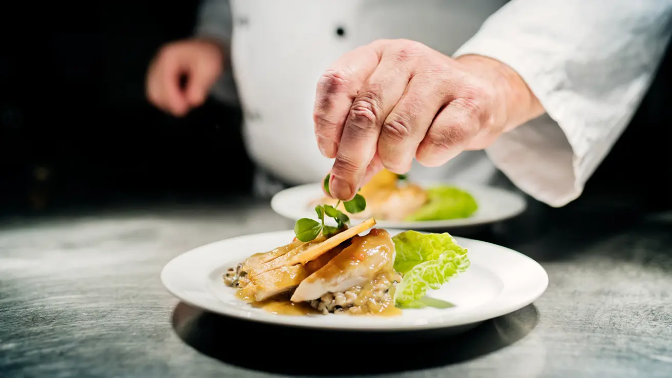 Kokk danderer en tallerken med risotto og kylling på kjøkkenet