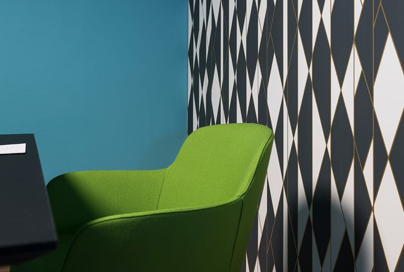 Møterom med mønstret svart og hvitt tapet og grønn stol  med blå vegg