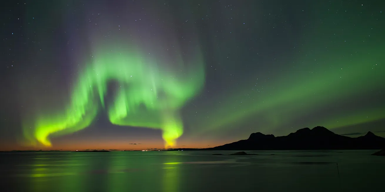 Dansende gr&oslash;nt nordlys p&aring; himmelen med litt orange nederst i horisonten.
