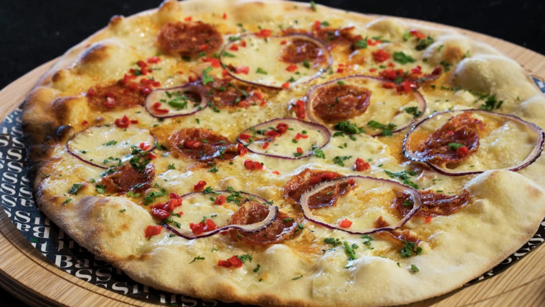 Generisk bilde av en italiensk pizza med pepperoni, ringer av rødløk, paprika, krydderplanter og ost.