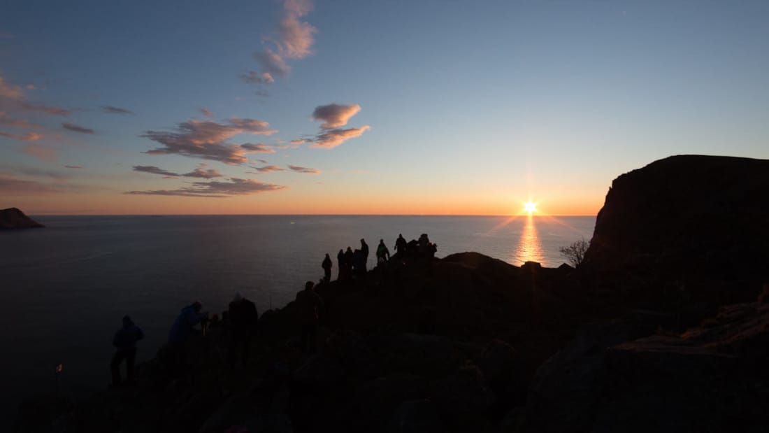 Mennesker står på en klippe og ser utover havet ved solnedgang.