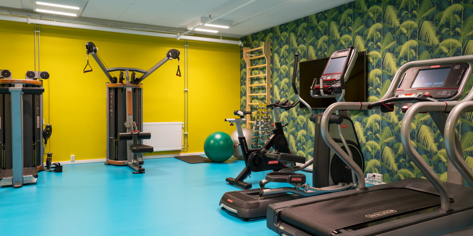 Treningsrom med gule vegger og turkis gulv med forskjellige treningsapparater på Thon Hotel Gardermoen