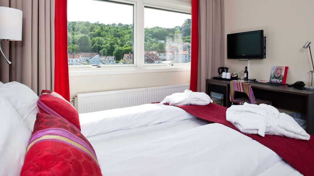 Superior rom med dekket seng og røde puter i lyst rom med TV
