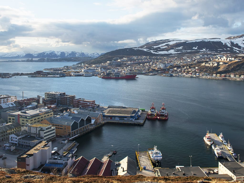 Hammerfest havn, med et stort vannområde som reflekterer den vakre himmelen og omgivelsene.
