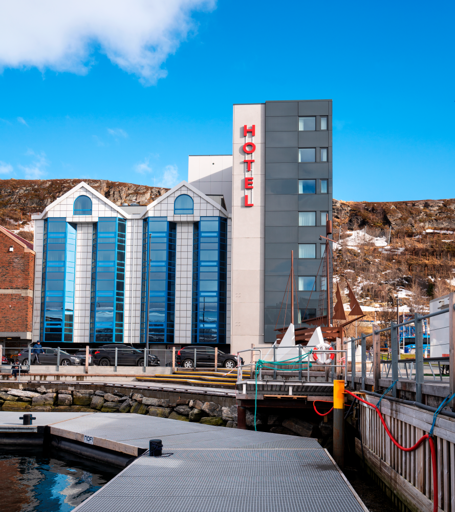 Fasaden til Thon Hotel Hammerfest sett fra havneområdet. Blå himmel i bakgrunnen. 