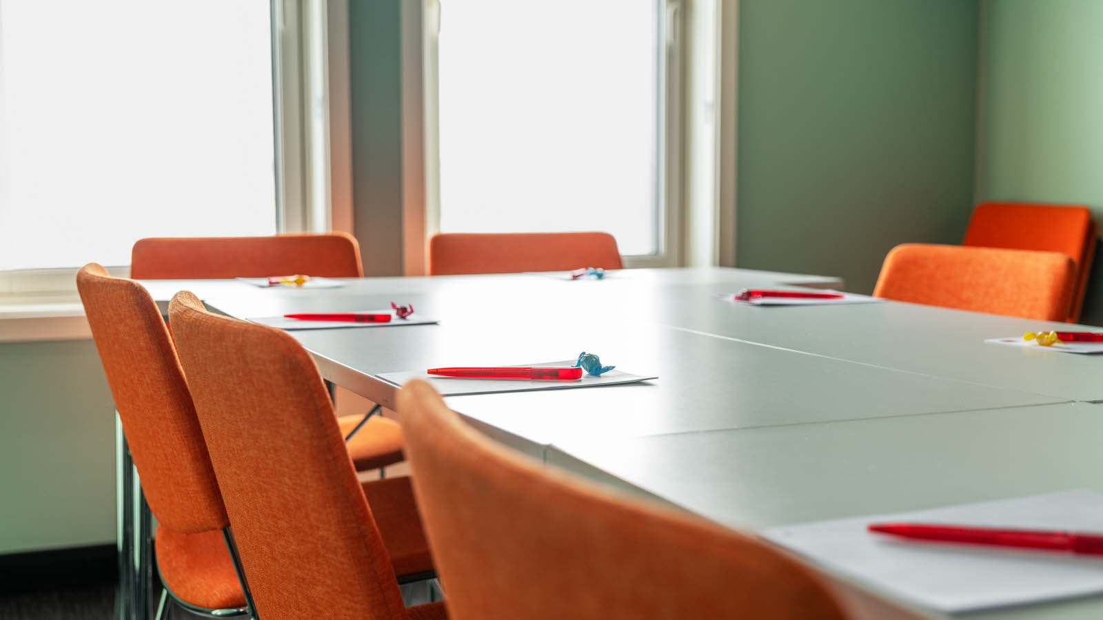 Detaljbilde av bord og oransje stoler på møterom med lys grønn farge på veggene 
