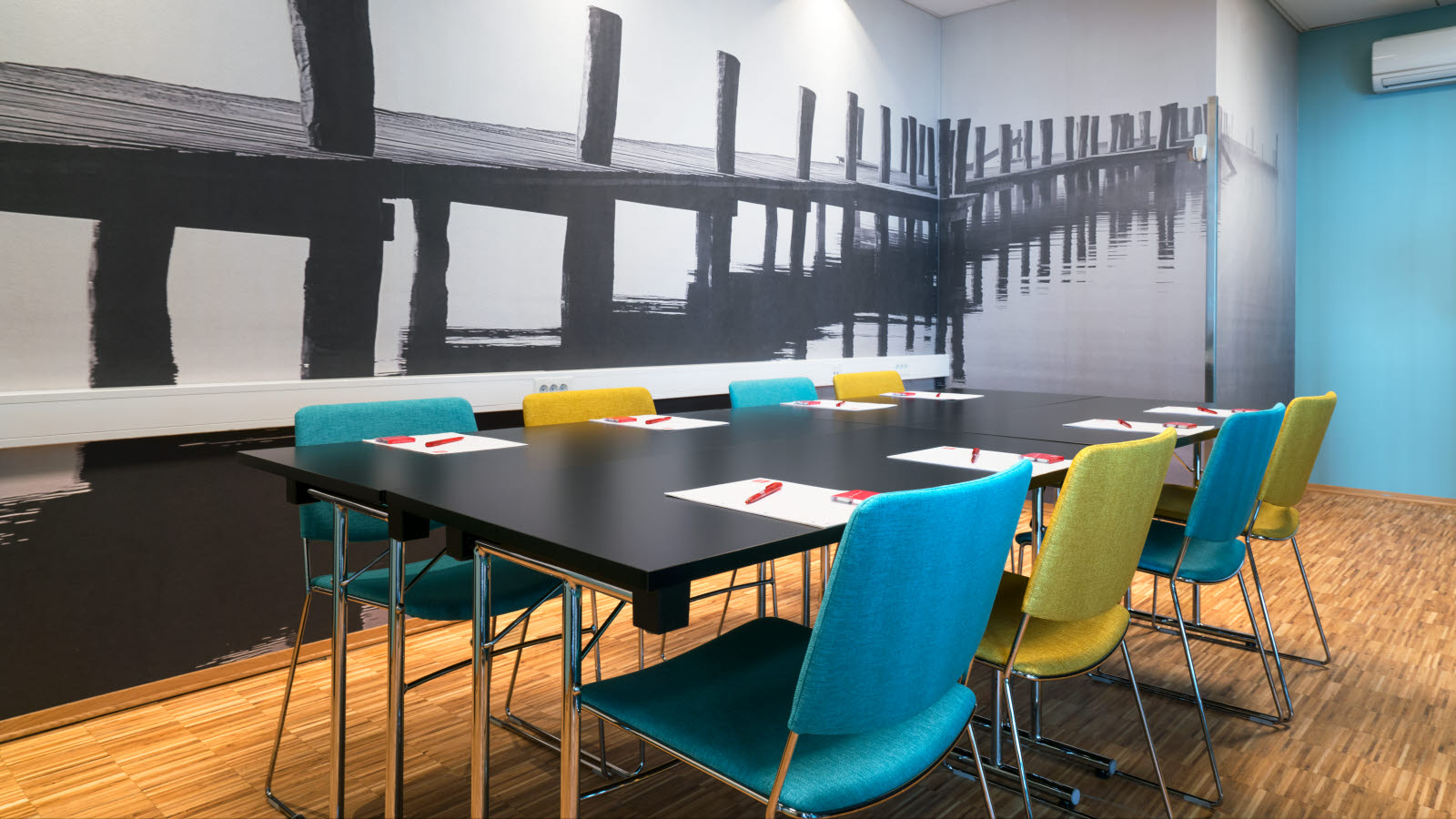 Møterom med fargerike stoler i styrebord med notatblokk og tapet på veggen av en brygge på Thon Hotel Kirkenes ved kaia i Kirkenes