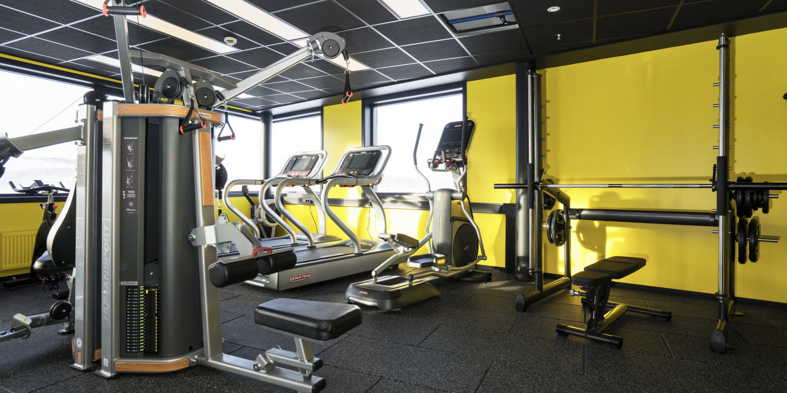 Treningsrom med forskjellige treningsapparater, gul vegg og utsikt fra vinduet på Thon Hotel Kirkenes ved kaia i Kirkenes sentrum