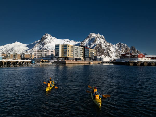 Fire personer fordelt på to kajakker padler inn mot Svolvær. I bakgrunnen ses Thon Hotel Svolvær og hotellets badstue.