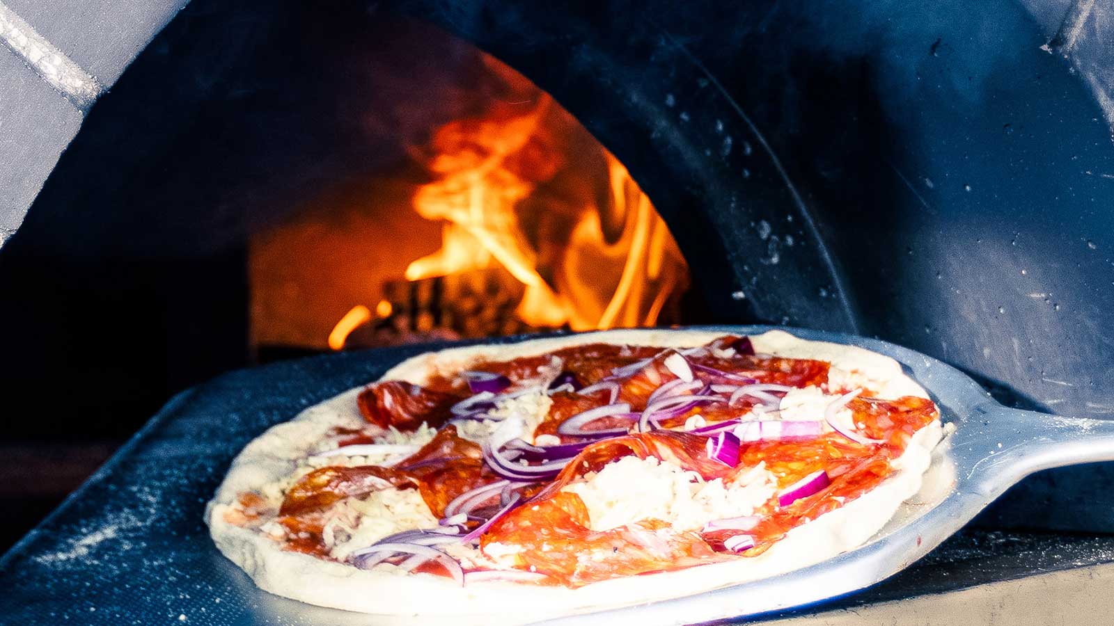 Pizza på vei inn i steinovn for steking.