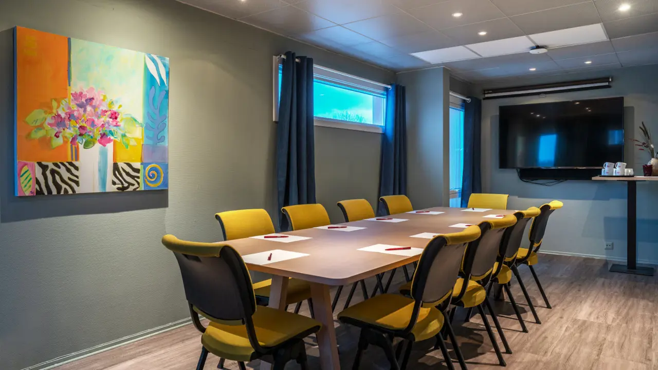 Møterom med 6 gule stoler i styrebordsoppsett, skjerm, vindu og parkettgulv.