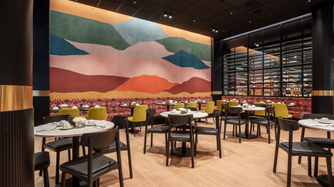Restaurant med fargerik vegg i bakgrunn og bord og stoler i front