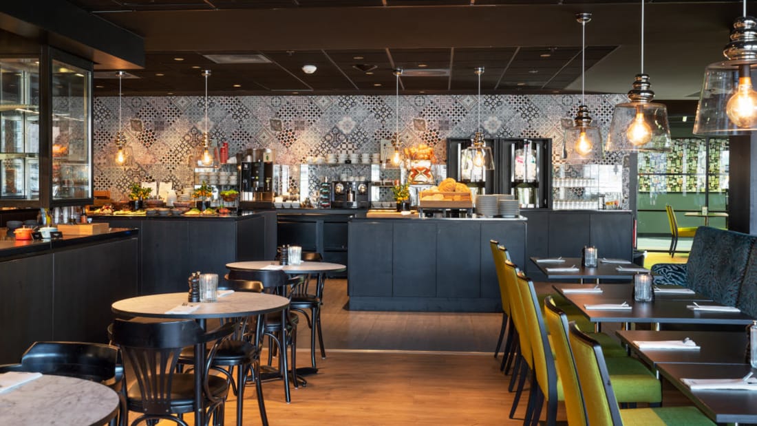 Restaurant med sitteplasser som ser mot kjøkken og buffetområdet med mønstrede fliser på veggen på Thon Hotel Triaden i Lørenskog