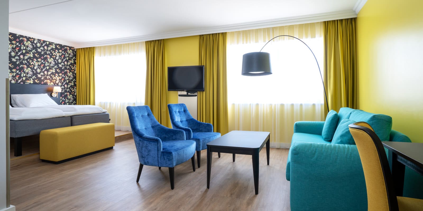 Dobbeltseng, mønstret tapet, tv, to lenestoler og sittegruppe i buisness room på Thon Hotel Triaden i Lørenskog