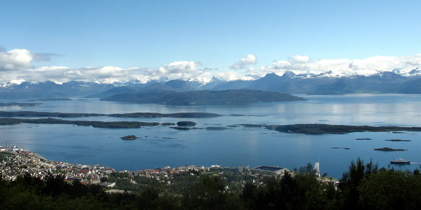 Molde sett fra oven med flotte fjell i horisonten, hvite skyer på himmelen og blått hav med bebyggelse i forkant.