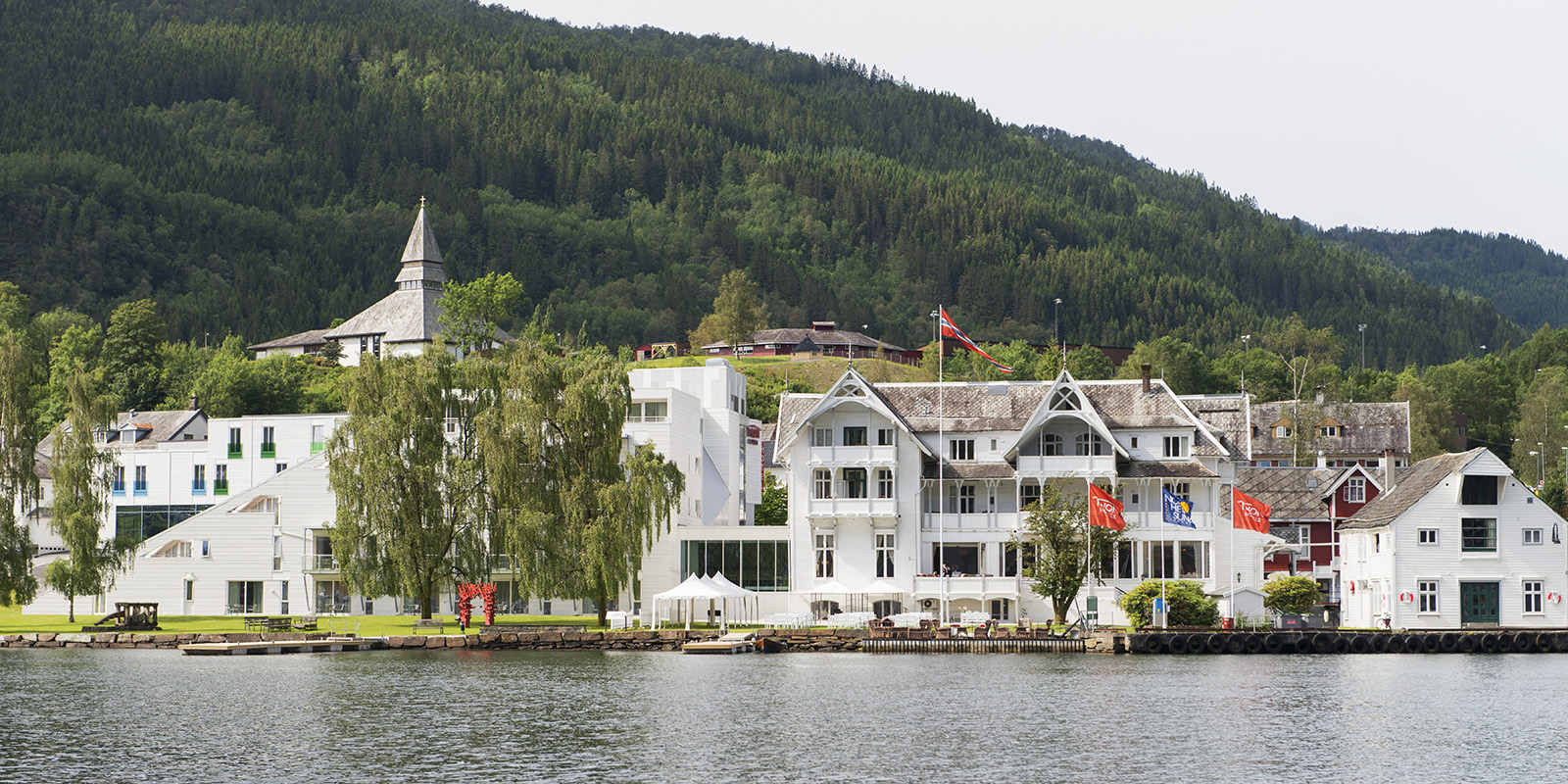 Fasaden på Thon Hotel Sandven sett fra vannet med fjellene i bakgrunnen