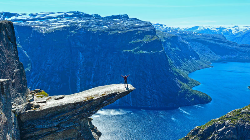 En person står ytterst på Trolltunga i strålende sol