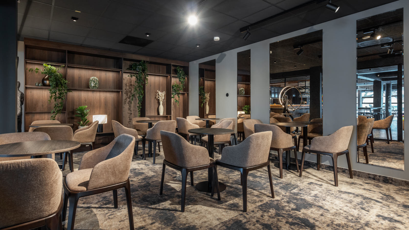 Lite møterom med teppegulv, store speil på veggen. Stoler rundt små svarte cafebord.