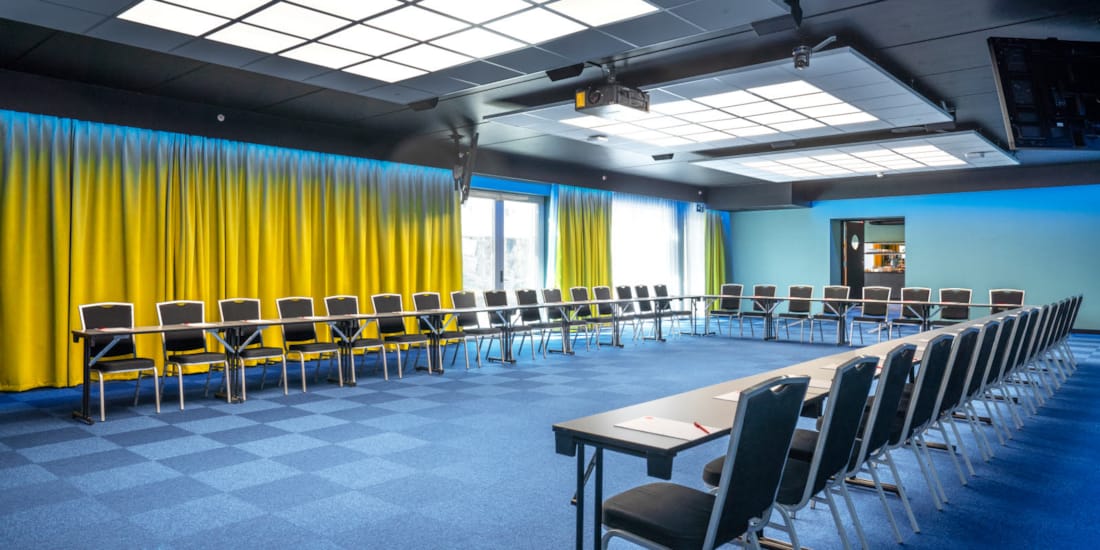 Konferansesal Bjerke satt opp i U-bord med plass til 52 stykker. Blå teppe, gule gardiner og prosjektor på Thon Hotel Linne i Oslo