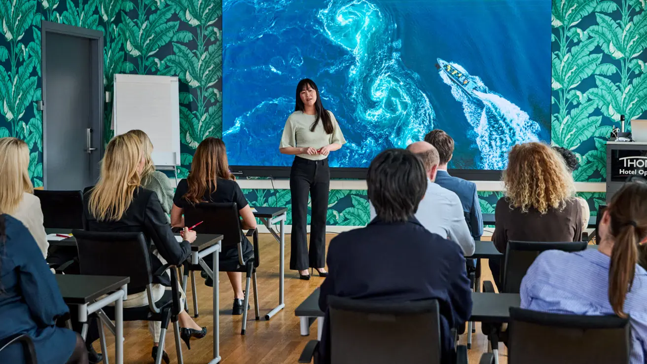 Fullsatt konferansesal, foredragsholder og lerret.