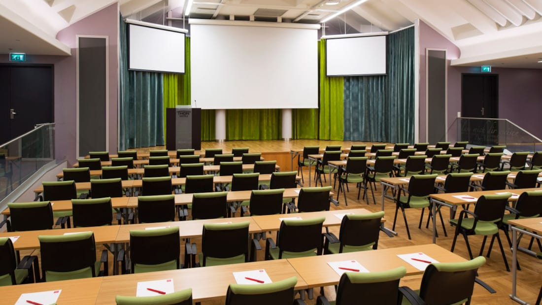 Stor konferanserom i klasseromsoppsett med tre projektorer og scene
