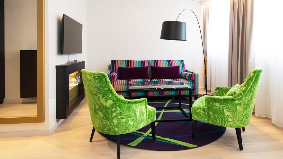 To grønne lenestoler og fargerik sofa ved siden av peis og TV