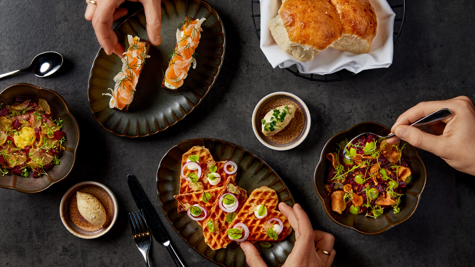 Utsnitt av flere småretter på et bord med mørk duk, sett ovenfra. 