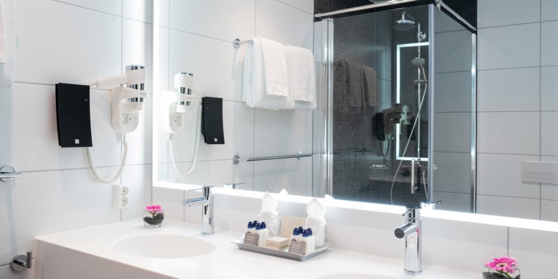 Dobbel servant og stort speil som reflekterer dusj på bad i suite på Thon Hotel Storo i Oslo