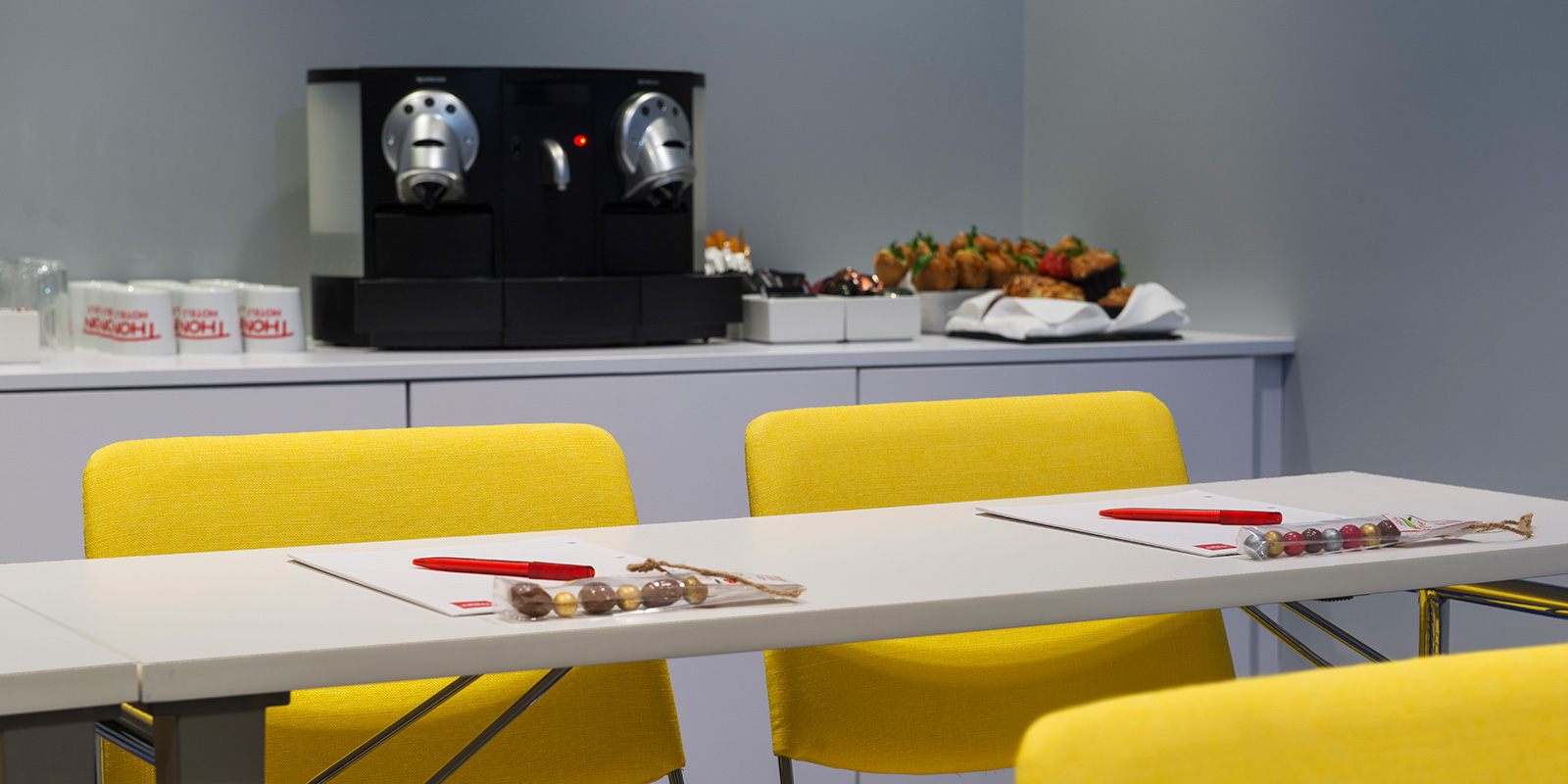 konferanse møterom bord og stoler, notatblokker, kaffe og snacks i bakgrunn