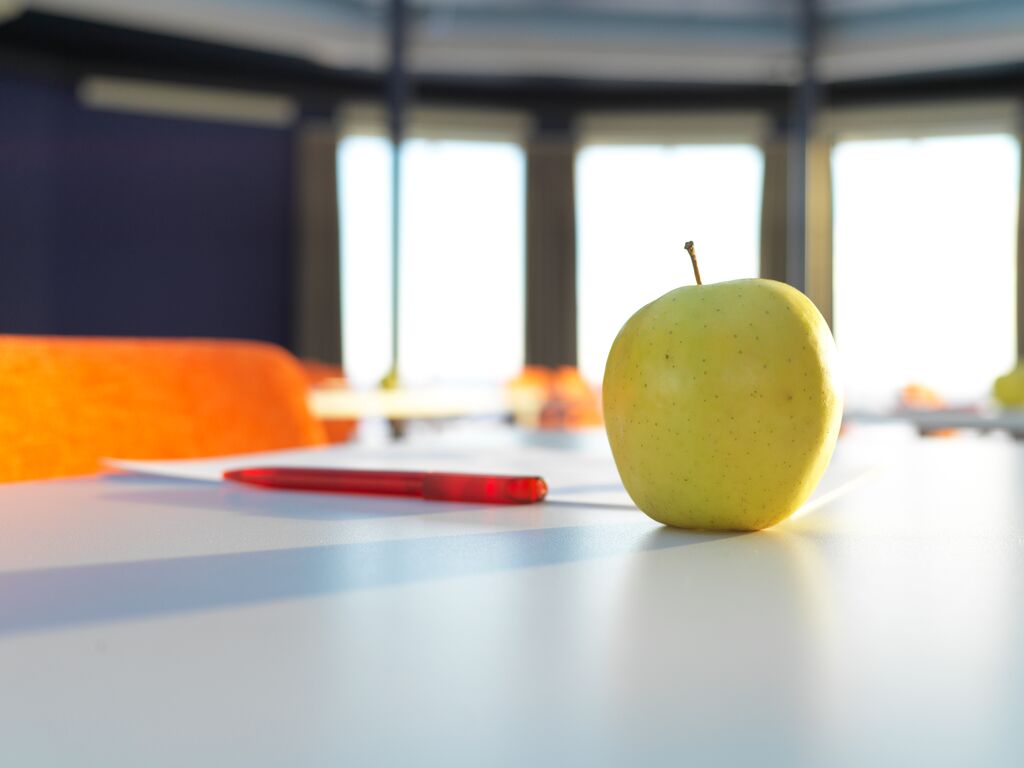 Nærbilde av et eple og en penn som ligger på et bord i et møterom.