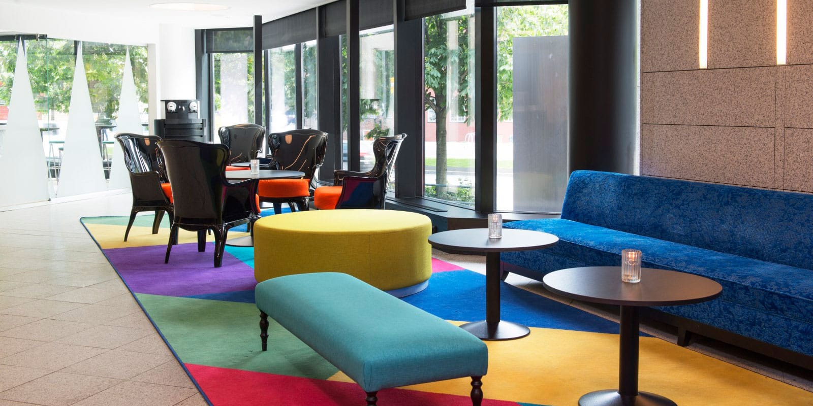 lobbyområde med sofa, sitteplasser og kafébord ved inngangsparti, fargerikt