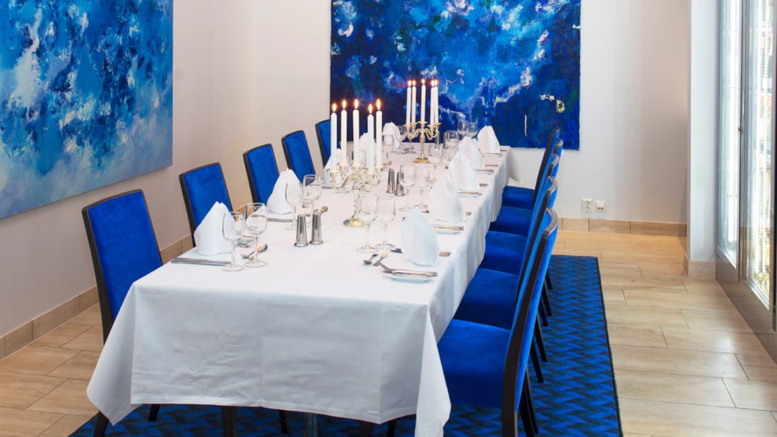 Møterom med langbord med blå stoler og malerier på veggen