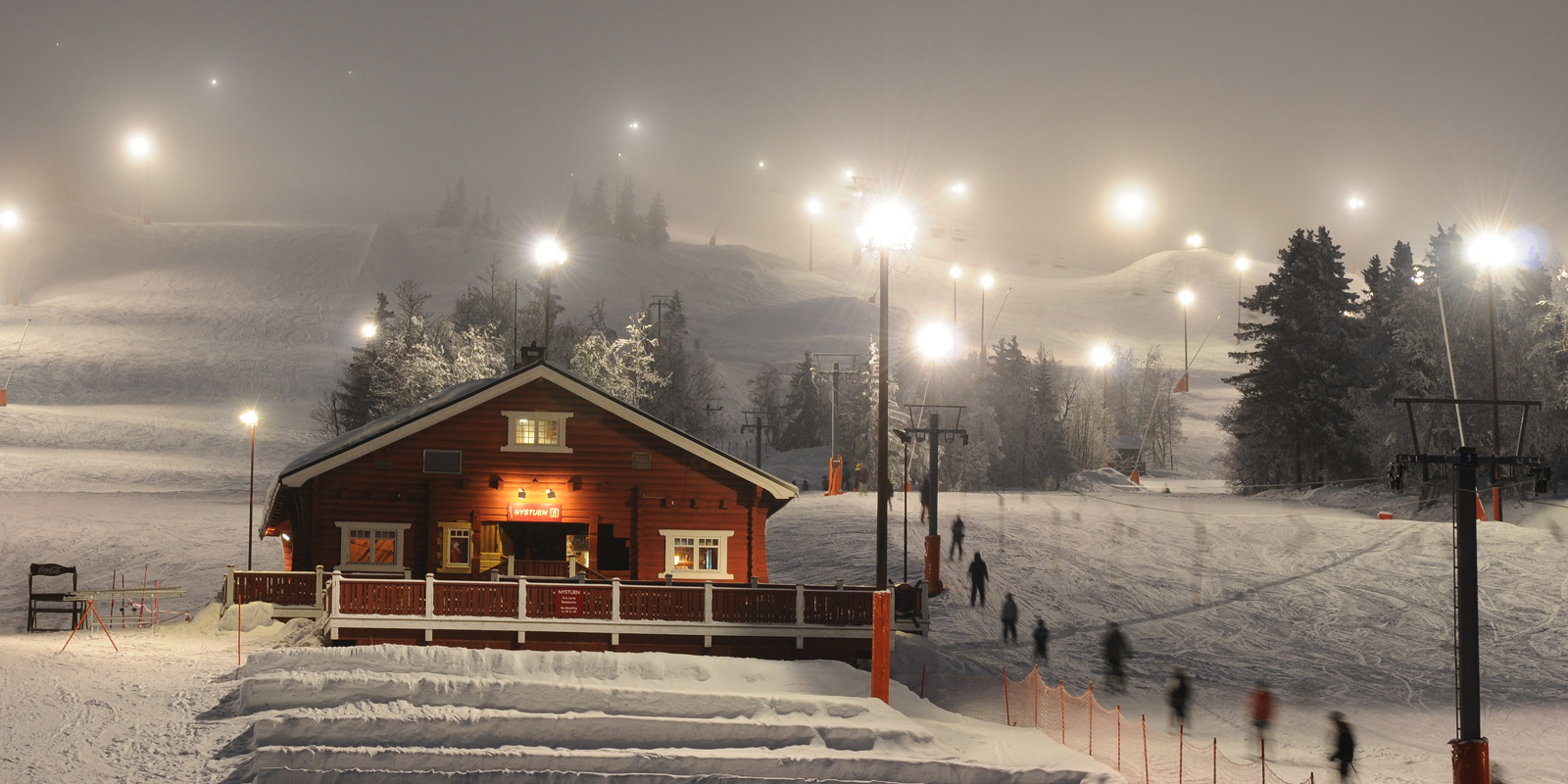 Kveld i skibakken lett tåke og lyse lamper med snødekket landskap
