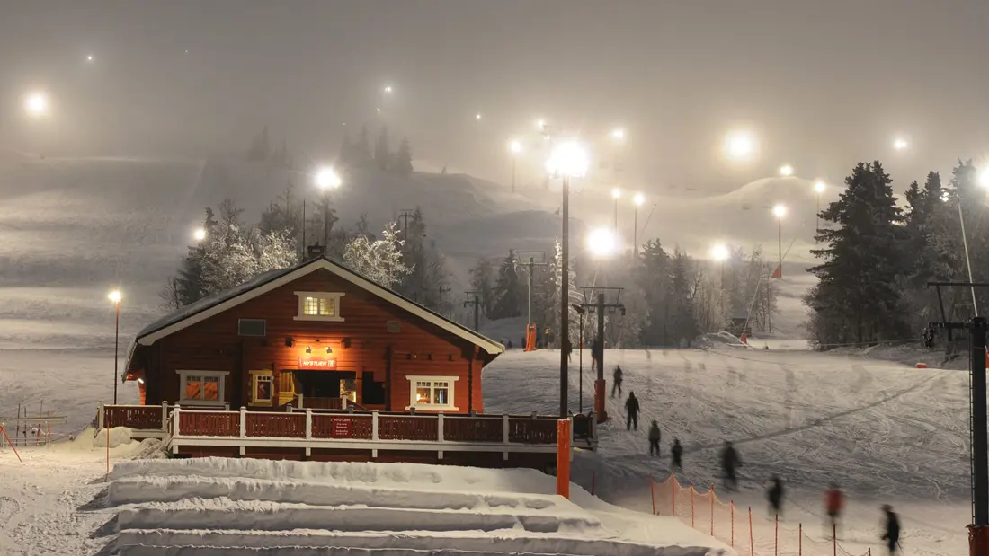 Kveld i skibakken lett tåke og lyse lamper med snødekket landskap